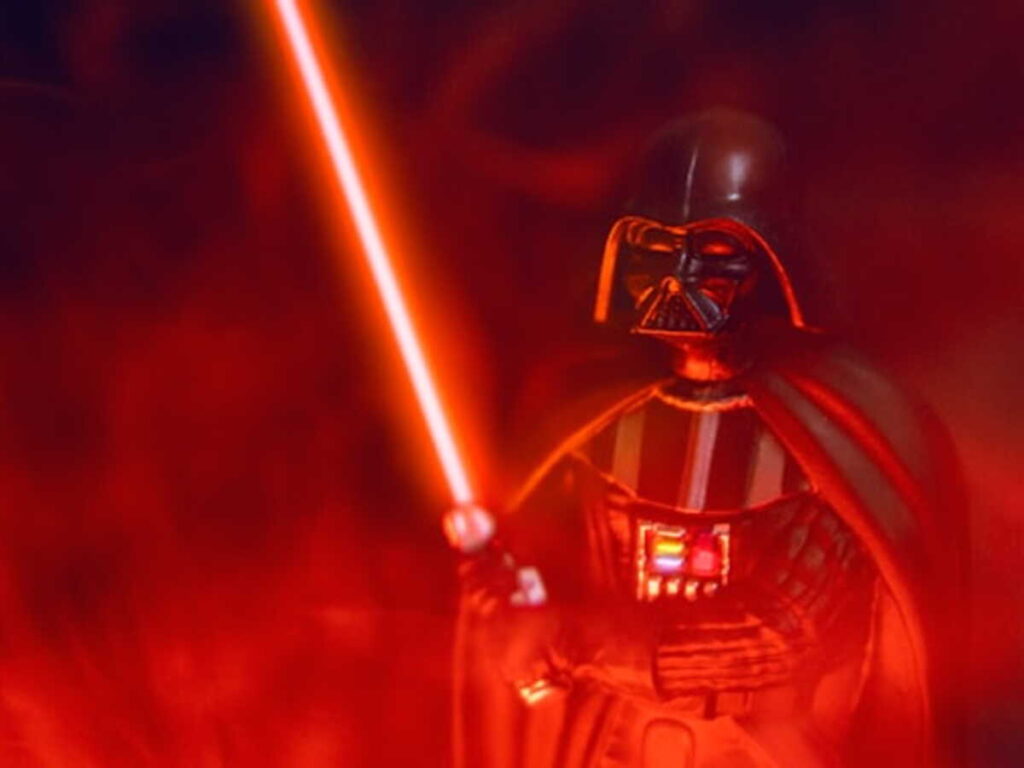 Un personnage en armure sombre avec une cape tient un sabre laser rouge au milieu d'un brouillard rouge, ressemblant fortement à Dark Vador de Star Wars, comme s'il sortait d'un film épique de science-fiction.