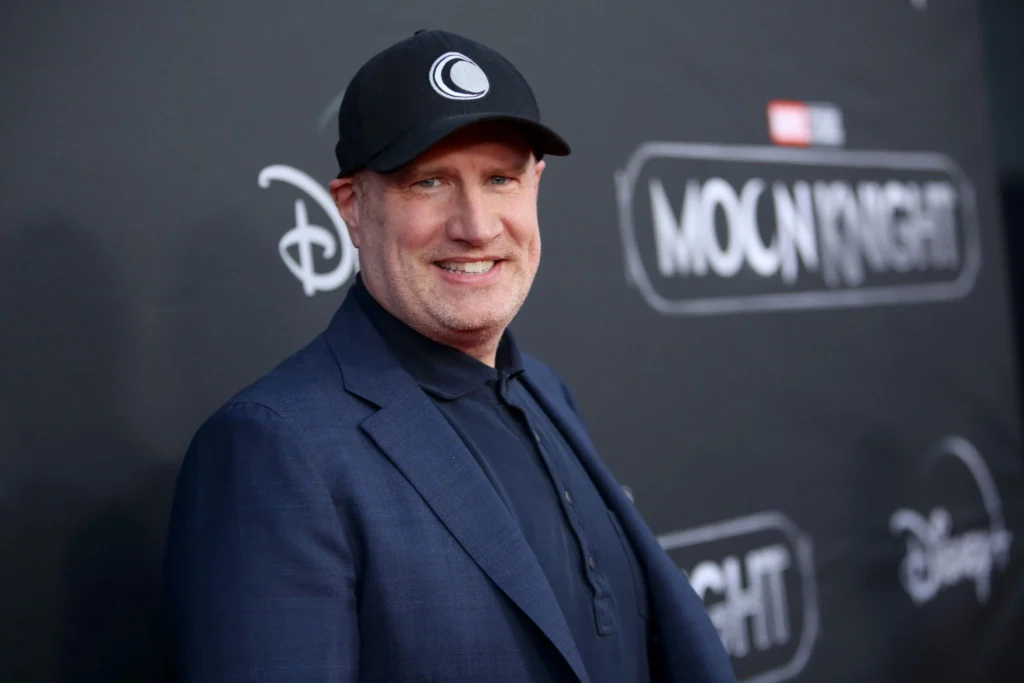 Un homme vêtu d'un blazer sombre et d'une casquette noire se tient devant une toile de fond de l'événement "Moon Knight" sur laquelle figurent les logos de Disney+ et de Marvel Studios.