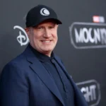 Un homme vêtu d'un blazer sombre et d'une casquette noire se tient devant une toile de fond de l'événement "Moon Knight" sur laquelle figurent les logos de Disney+ et de Marvel Studios.