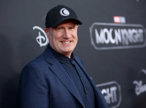 Un homme vêtu d'un blazer sombre et d'une casquette noire se tient devant une toile de fond de l'événement "Moon Knight" sur laquelle figurent les logos de Disney+ et de Marvel Studios.