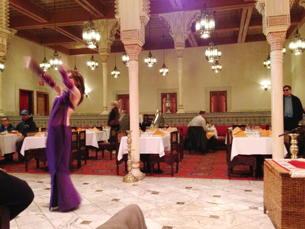 Une danseuse du ventre vêtue d'un costume violet se produit au restaurant Marrakesh du pavillon du Maroc, enchantant les convives au milieu de colonnes ornées, de lustres étincelants et de tables élégantes à Disney World Orlando.