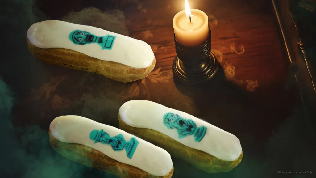 Trois éclairs au glaçage blanc et aux visages imprimés en bleu sont disposés à côté d'une bougie allumée sur une surface en bois au fond enfumé, évoquant l'esprit fantaisiste de la Parade Mickey à Disneyland Paris.