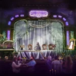 Une salle ornée et faiblement éclairée de Disneyland Paris présente une table décorée sur une scène, un piano, des couronnes festives et un portrait inquiétant - capturant l'esprit d'Halloween Disney 2025 - avec des invités assis au premier plan.