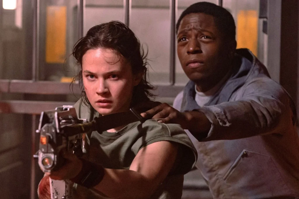 Deux personnes se tiennent l'une à côté de l'autre dans une scène tendue d'Alien Romulus ; celle qui est devant pointe une arme tandis que l'autre se tient derrière, toutes deux semblant alertes et concentrées - un moment saisissant dans la dernière production Disney de Fede Álvarez.