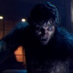 Une personne aux traits de loup-garou, rappelant le loup-garou de nuit du MCU de Marvel, est accroupie avec une expression intense dans une pièce faiblement éclairée.