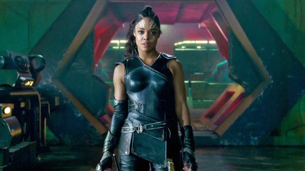 Un personnage puissant en armure noire futuriste se tient avec assurance devant une grande porte hexagonale, évoquant l'aura de Valkyrie Marvel et laissant entrevoir des origines mystérieuses dans ce décor de science-fiction.