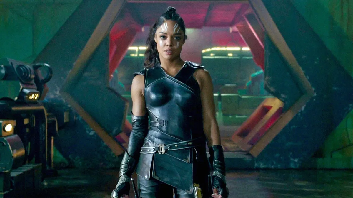 Un personnage puissant en armure noire futuriste se tient avec assurance devant une grande porte hexagonale, évoquant l'aura de Valkyrie Marvel et laissant entrevoir des origines mystérieuses dans ce décor de science-fiction.