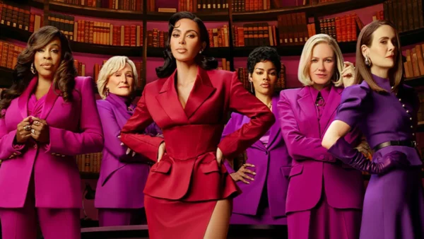 Six femmes se tiennent avec assurance devant des étagères, l'une d'entre elles en tailleur rouge au centre et les autres en tailleur violet assorti à ses côtés. Il s'agit d'une scène de responsabilisation tirée de la prochaine série Disney+ de Kim Kardashian, All's Fair.
