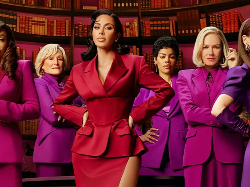Six femmes se tiennent avec assurance devant des étagères, l'une d'entre elles en tailleur rouge au centre et les autres en tailleur violet assorti à ses côtés. Il s'agit d'une scène de responsabilisation tirée de la prochaine série Disney+ de Kim Kardashian, All's Fair.