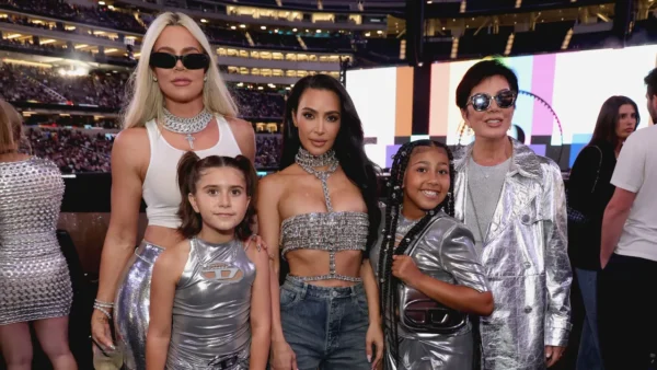 Cinq personnes se tiennent ensemble lors d'un événement. Trois adultes et deux enfants portent des tenues métalliques ou étincelantes, comme dans une scène de Kardashian Saison 7. En arrière-plan, on aperçoit la foule d'un stade.