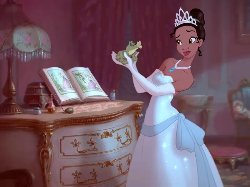 Une femme animée ressemblant à Tiana de Disney, vêtue d'une robe blanche et d'un diadème, tient une grenouille, debout à côté d'un bureau orné d'un livre ouvert - parfait pour une liste de naissance magique, dans une pièce élégante faiblement éclairée.