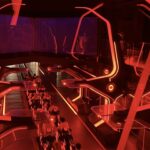Une aire de lancement de montagnes russes intérieures futuristes s'illumine de néons rouge vif, avec des structures angulaires et des véhicules de type moto sur une piste inspirée du Lightcycle Run de Tron.