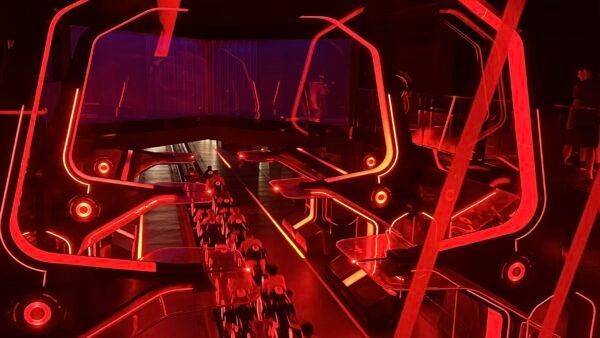 Une aire de lancement de montagnes russes intérieures futuristes s'illumine de néons rouge vif, avec des structures angulaires et des véhicules de type moto sur une piste inspirée du Lightcycle Run de Tron.