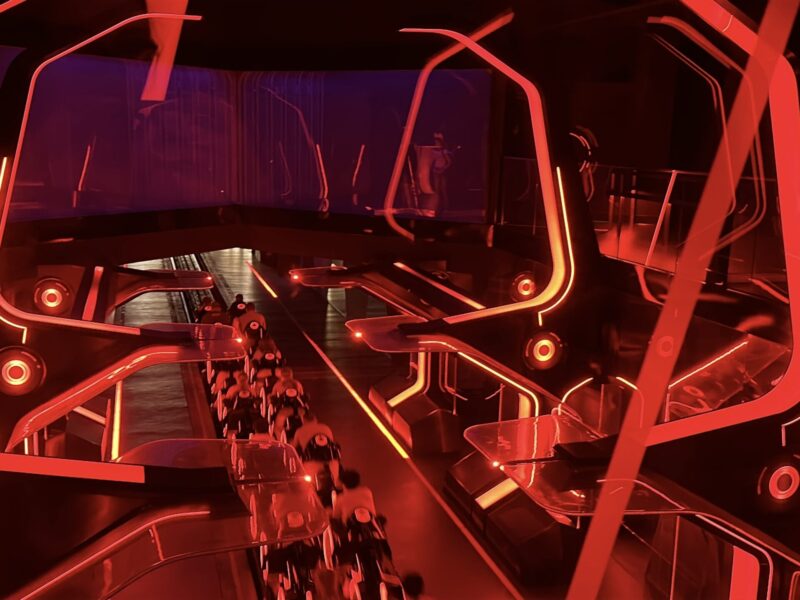 Une aire de lancement de montagnes russes intérieures futuristes s'illumine de néons rouge vif, avec des structures angulaires et des véhicules de type moto sur une piste inspirée du Lightcycle Run de Tron.