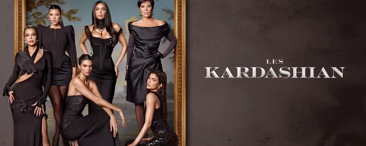 Six femmes en tenue de soirée noire posent devant un grand cadre orné sur un fond neutre avec le texte "Les Kardashian" à côté d'elles, teasing la bande-annonce de Kardashian Saison 7 sur Disney+.