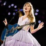 Une femme vêtue d'une robe lavande chante sur scène, jouant d'une guitare acoustique bleue sous les lumières de la scène, capturant ainsi une ambiance magique de ciné-concert, parfaite pour tout fan de Disney+ ou de Taylor Swift.