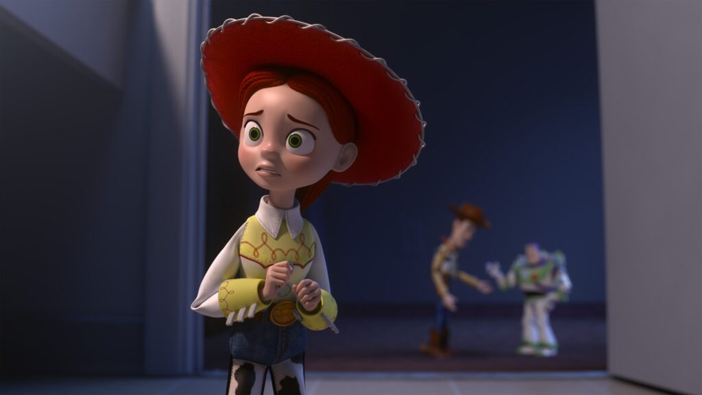 Le personnage animé Jessie, avec son chapeau rouge et sa tenue de western, se tient inquiet au premier plan, tandis que deux personnages flous interagissent derrière elle - ce qui laisse présager une nouvelle aventure entre jouets et technologie dans Toy Story 5.