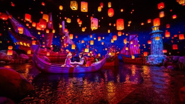 Un couple est assis dans un bateau sur un lac à Tokyo Disneyland, entouré de lanternes flottantes, de bateaux illuminés et d'un phare sous un ciel étoilé dans l'une des attractions les plus populaires du parc.