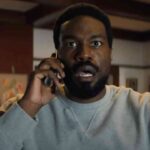 Un homme à l'expression surprise porte un téléphone à l'oreille alors qu'il se trouve à l'intérieur d'une pièce dont les murs sont ornés d'œuvres d'art, comme s'il réagissait à une nouvelle inattendue concernant la prochaine série Marvel de Wonder Man sur Disney+.