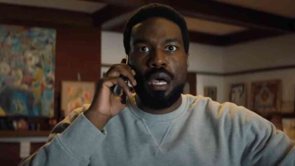 Un homme à l'expression surprise porte un téléphone à l'oreille alors qu'il se trouve à l'intérieur d'une pièce dont les murs sont ornés d'œuvres d'art, comme s'il réagissait à une nouvelle inattendue concernant la prochaine série Marvel de Wonder Man sur Disney+.