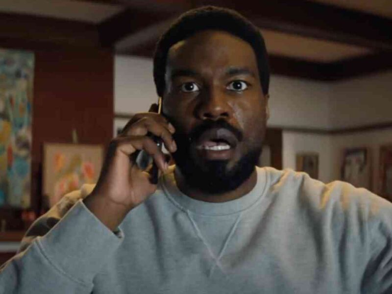 Un homme à l'expression surprise porte un téléphone à l'oreille alors qu'il se trouve à l'intérieur d'une pièce dont les murs sont ornés d'œuvres d'art, comme s'il réagissait à une nouvelle inattendue concernant la prochaine série Marvel de Wonder Man sur Disney+.