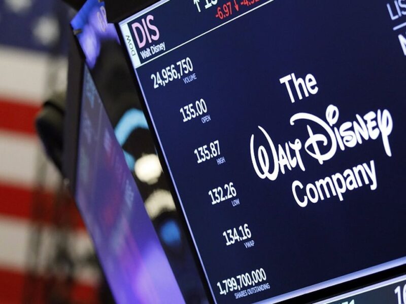 Un écran de la Bourse de New York montre le logo de Disney, des données boursières reflétant les résultats décevants et un drapeau américain en arrière-plan.