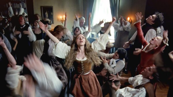 Un groupe de personnes en tenue historique se tient dans une pièce, beaucoup avec les bras levés et des visages expressifs, tandis qu'une femme au centre - évoquant Amanda Seyfried dans un biopic - regarde vers le haut. Inspiré par Le Testament D'Ann Lee.