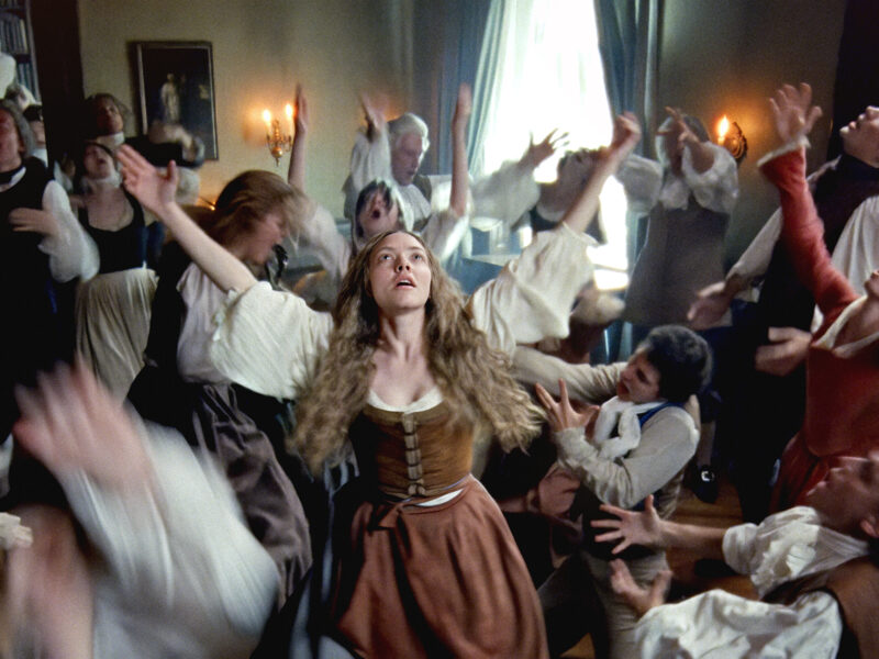 Un groupe de personnes en tenue historique se tient dans une pièce, beaucoup avec les bras levés et des visages expressifs, tandis qu'une femme au centre - évoquant Amanda Seyfried dans un biopic - regarde vers le haut. Inspiré par Le Testament D'Ann Lee.