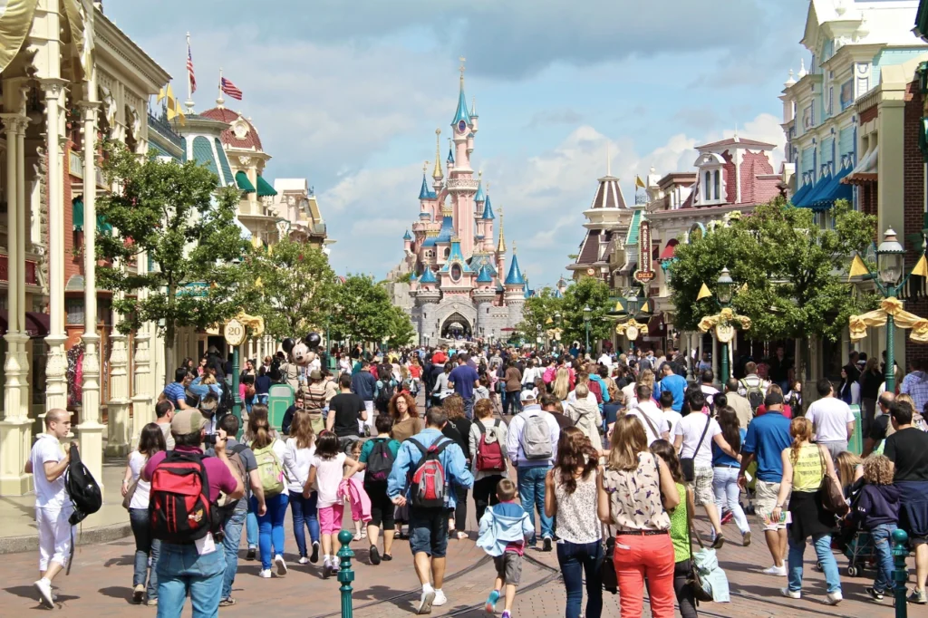 Une foule de personnes descendent une rue à thème en direction d'un château du parc Disneyland par une journée ensoleillée, en vérifiant le temps d'attente Disneyland pour profiter au maximum de leur visite et minimiser le temps passé dans un éventuel fichier d'attente Disneyland.