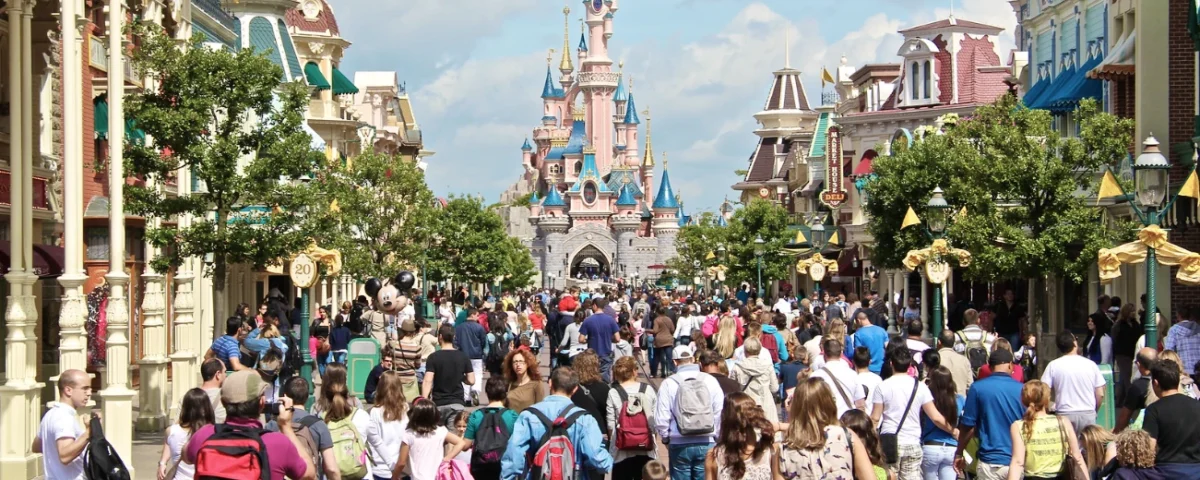 Une foule de personnes descendent une rue à thème en direction d'un château du parc Disneyland par une journée ensoleillée, en vérifiant le temps d'attente Disneyland pour profiter au maximum de leur visite et minimiser le temps passé dans un éventuel fichier d'attente Disneyland.