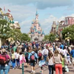 Une foule de personnes descendent une rue à thème en direction d'un château du parc Disneyland par une journée ensoleillée, en vérifiant le temps d'attente Disneyland pour profiter au maximum de leur visite et minimiser le temps passé dans un éventuel fichier d'attente Disneyland.