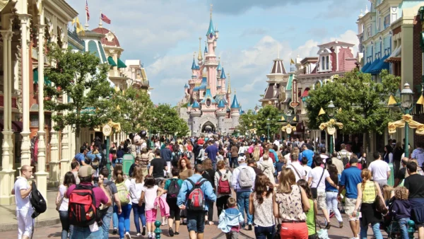 Une foule de personnes descendent une rue à thème en direction d'un château du parc Disneyland par une journée ensoleillée, en vérifiant le temps d'attente Disneyland pour profiter au maximum de leur visite et minimiser le temps passé dans un éventuel fichier d'attente Disneyland.