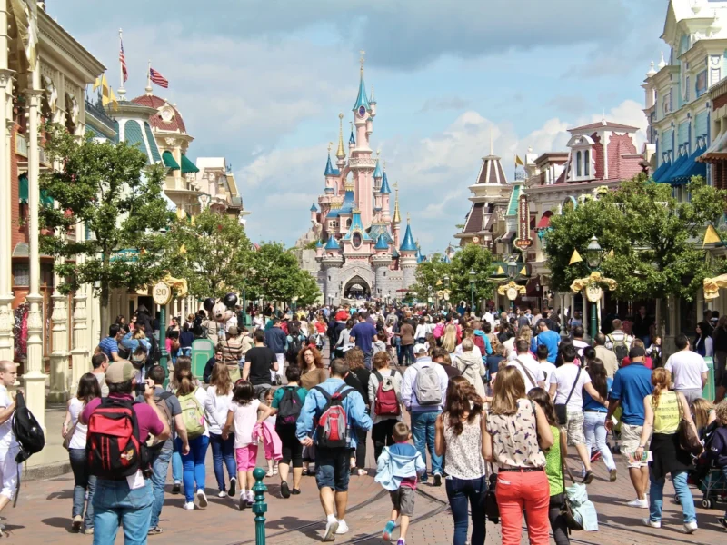 Une foule de personnes descendent une rue à thème en direction d'un château du parc Disneyland par une journée ensoleillée, en vérifiant le temps d'attente Disneyland pour profiter au maximum de leur visite et minimiser le temps passé dans un éventuel fichier d'attente Disneyland.