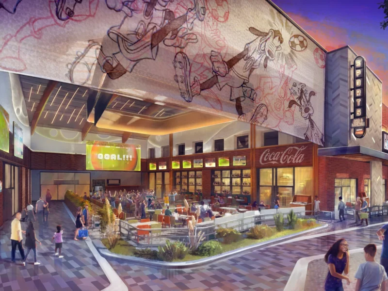 Place extérieure à Disney Village, où les gens se promènent et mangent sous de grands écrans sportifs numériques, des peintures murales d'animaux de dessins animés et une enseigne Coca-Cola sur un bâtiment moderne - vivez la magie alors que Disneyland Paris se dirige vers ses rénovations 2026.