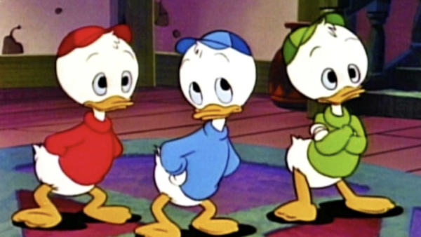 Trois canetons de dessin animé, dont Riri, portent des chemises et des casquettes rouges, bleues et vertes. Ils se tiennent à l'intérieur, les mains derrière le dos, face à l'avant.