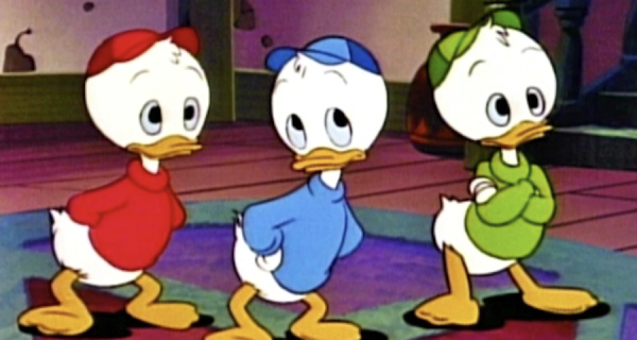 Trois canetons de dessin animé, dont Riri, portent des chemises et des casquettes rouges, bleues et vertes. Ils se tiennent à l'intérieur, les mains derrière le dos, face à l'avant.