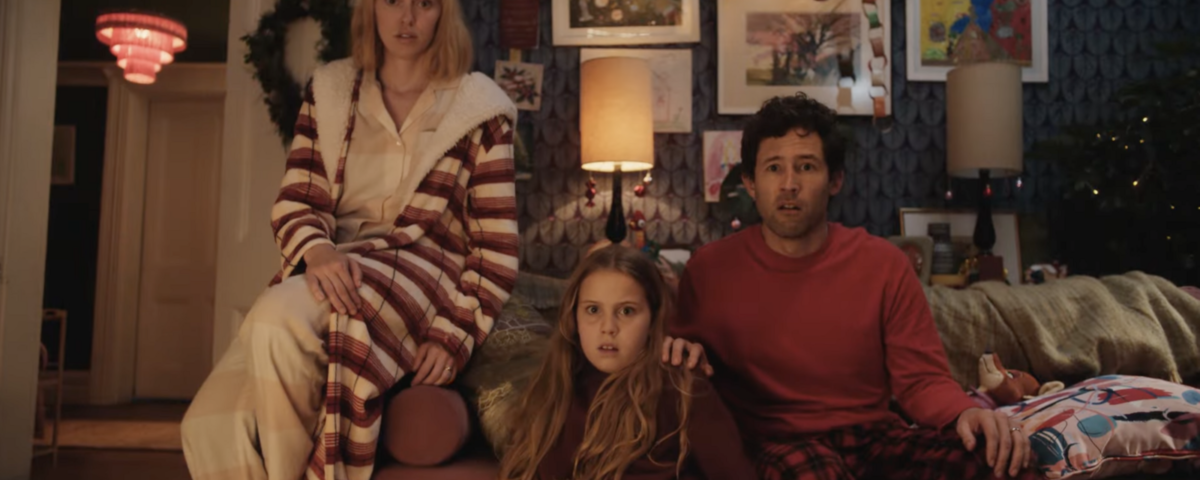 Une femme, un homme et une jeune fille sont assis sur le canapé d'un salon, l'air surpris. La pièce est décorée d'œuvres d'art et de couronnes de Noël pour Le Plus Beau Des Noëls, inspiré de la magie du Court-métrage Noël Disney.