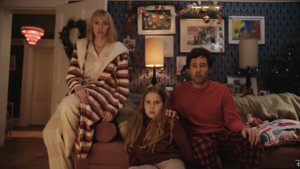 Une femme, un homme et une jeune fille sont assis sur le canapé d'un salon, l'air surpris. La pièce est décorée d'œuvres d'art et de couronnes de Noël pour Le Plus Beau Des Noëls, inspiré de la magie du Court-métrage Noël Disney.