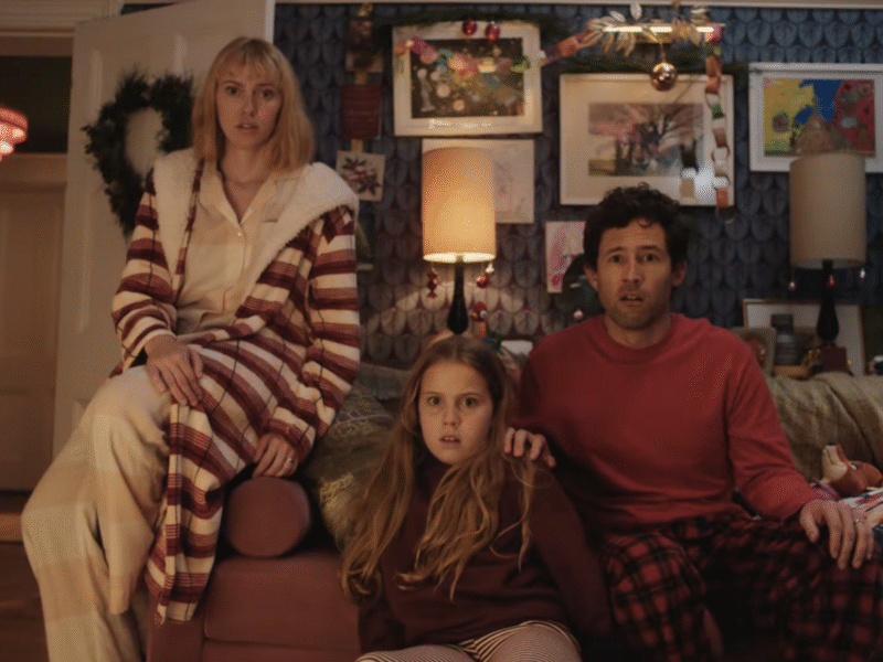 Une femme, un homme et une jeune fille sont assis sur le canapé d'un salon, l'air surpris. La pièce est décorée d'œuvres d'art et de couronnes de Noël pour Le Plus Beau Des Noëls, inspiré de la magie du Court-métrage Noël Disney.