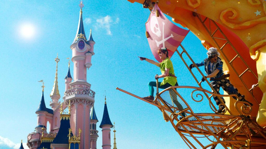 Un char coloré de la parade avec Peter Pan et un pirate en costume passe devant un château rose sous un ciel bleu vif, rendant votre séjour à Disneyland Paris vraiment magique.
