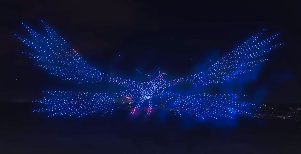 Des centaines de drones éclairés en bleu et en rouge à Disneyland Paris forment la forme d'un grand oiseau aux ailes déployées dans un ciel nocturne sombre, évoquant le monde envoûtant d'Avatar au-dessus du Parc Walt Disney Studios.