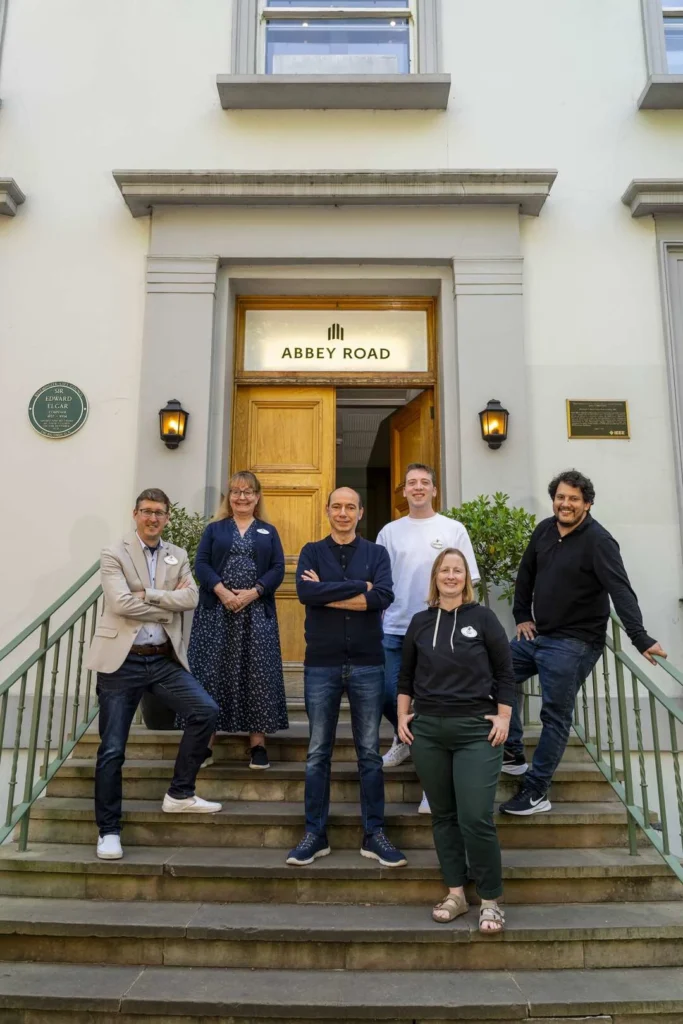 Six personnes se tiennent sur les marches des studios Abbey Road, posant pour une photo de groupe devant la porte principale du bâtiment, où Philippe Rombi a enregistré la musique originale pour Disney Adventure World.