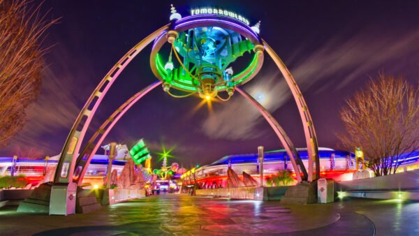 L'entrée de Tomorrowland, de nuit, avec une grande enseigne lumineuse et des arches futuristes aux lumières colorées, illustre l'esprit d'innovation de Disney, avec un monorail glissant en arrière-plan.