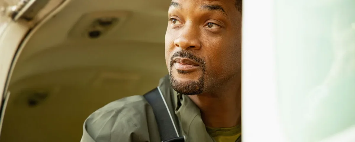 Un homme vêtu d'une veste verte avec une sangle sur l'épaule regarde pensivement par la portière ouverte d'un véhicule, une douce lumière naturelle illuminant son visage, évoquant l'esprit d'aventure de Nat Geo sur Disney+.