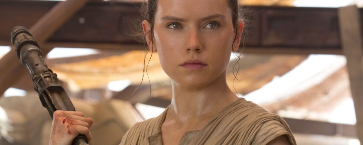 Une femme vêtue d'une tenue bronzée, rappelant le rôle emblématique de Daisy Ridley, se tient debout en tenant un bâton et regarde devant elle avec détermination dans un décor rustique et ensoleillé, évoquant l'esprit du Nouvel Ordre Jedi de La Guerre des étoiles 10.