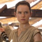 Une femme vêtue d'une tenue bronzée, rappelant le rôle emblématique de Daisy Ridley, se tient debout en tenant un bâton et regarde devant elle avec détermination dans un décor rustique et ensoleillé, évoquant l'esprit du Nouvel Ordre Jedi de La Guerre des étoiles 10.
