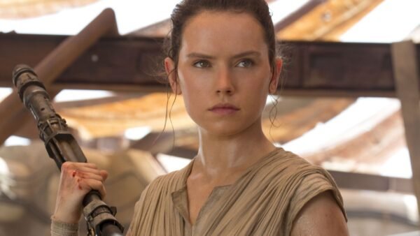 Une femme vêtue d'une tenue bronzée, rappelant le rôle emblématique de Daisy Ridley, se tient debout en tenant un bâton et regarde devant elle avec détermination dans un décor rustique et ensoleillé, évoquant l'esprit du Nouvel Ordre Jedi de La Guerre des étoiles 10.