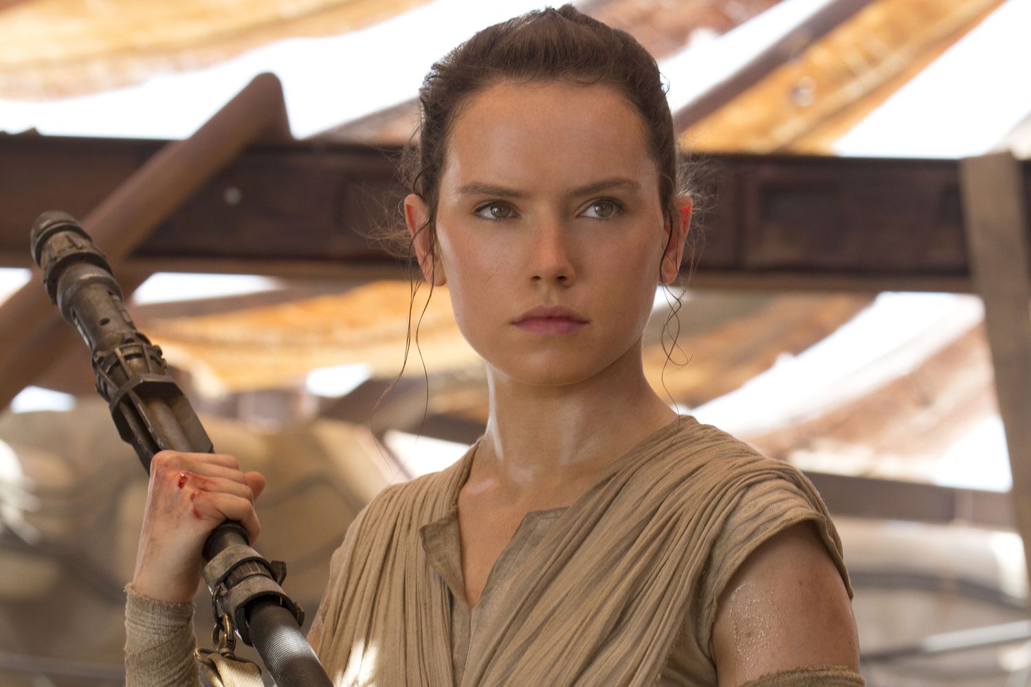 Une femme vêtue d'une tenue bronzée, rappelant le rôle emblématique de Daisy Ridley, se tient debout en tenant un bâton et regarde devant elle avec détermination dans un décor rustique et ensoleillé, évoquant l'esprit du Nouvel Ordre Jedi de La Guerre des étoiles 10.