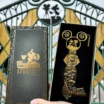 Une main tient une boîte Walt Disney Studios Édition Limitée et un grand Clé Collector Jumbo devant la porte d'entrée emblématique du studio.