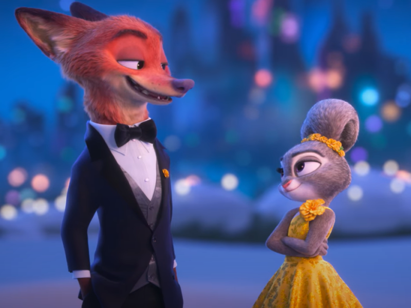 Un renard en smoking noir et un lapin en robe jaune se tiennent côte à côte, l'un face à l'autre, avec un paysage urbain flou en arrière-plan. Cette image illustre le charme de Zootopie 2 de Disney et l'engouement qu'il devrait susciter au box-office.